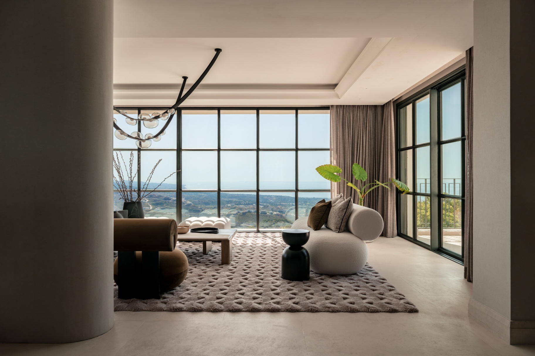 A lounge at Casa Servetta with floor-to-ceiling windows opening toward the valley and sea at dusk.