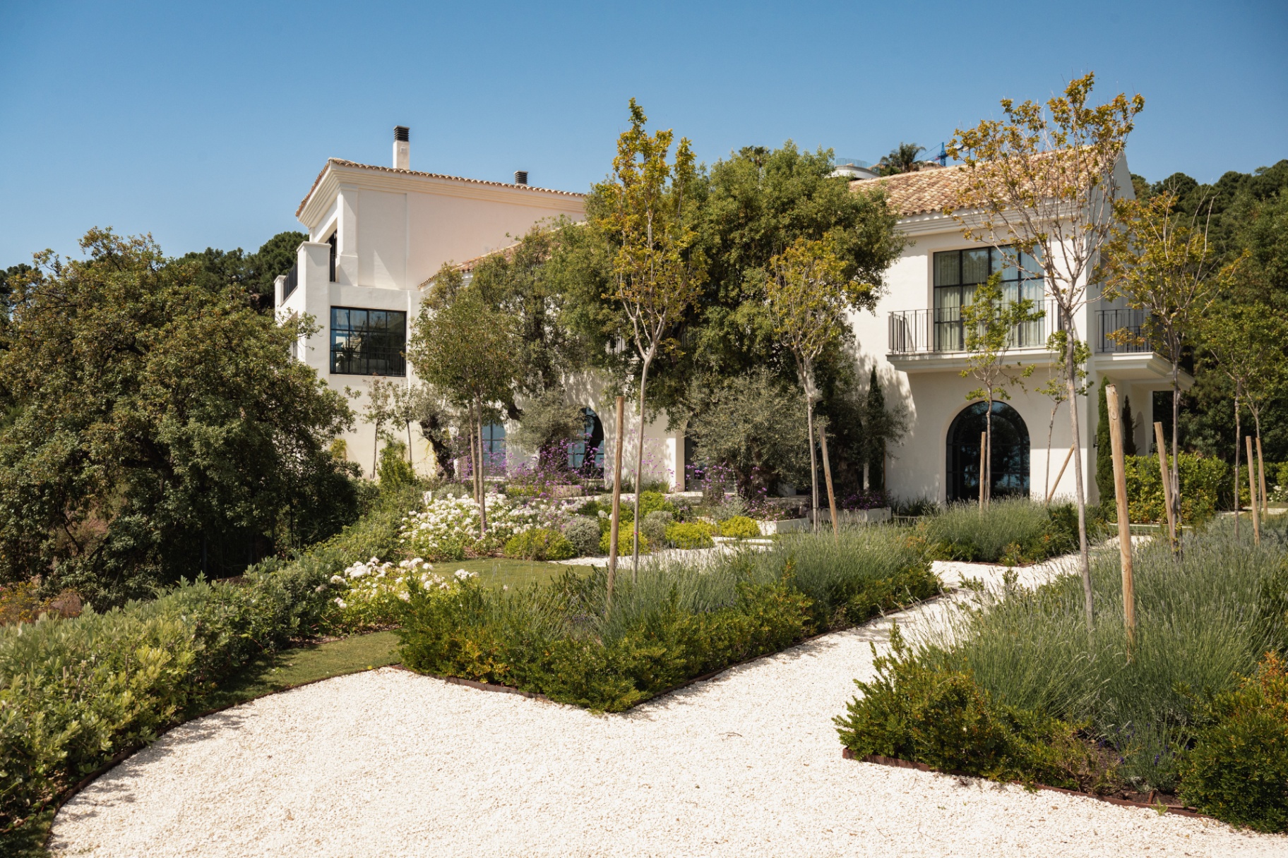 The gardens of Casa Servetta with white facades, mature trees and gravel paths.