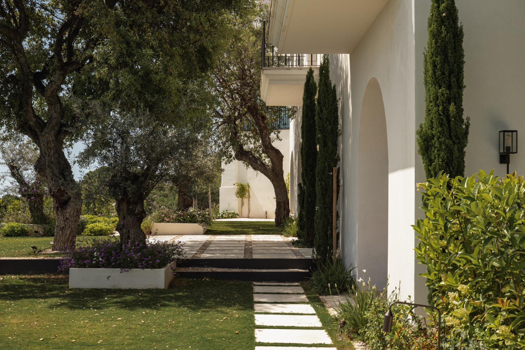 Cypresses and olive trees along the villa's arched garden facade.