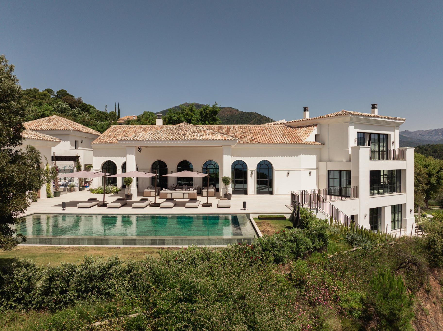 Wide view of the villa, terrace and infinity pool from the garden.
